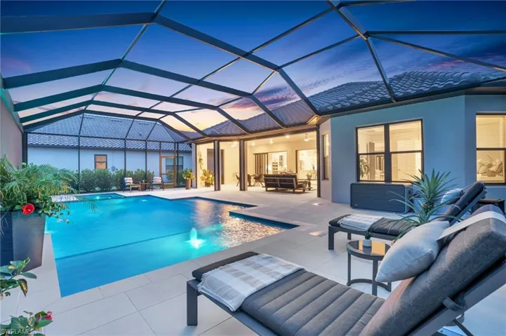 Pool at dusk featuring an outdoor hangout area, glass enclosure, a patio, and pool water feature