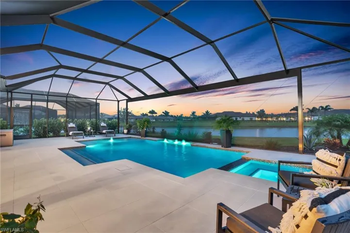 Pool at dusk featuring a water view, an in ground hot tub, a patio area, and glass enclosure