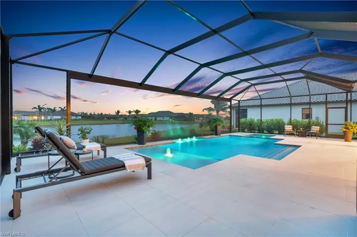 Pool at dusk featuring a lanai, a patio, and a water view
