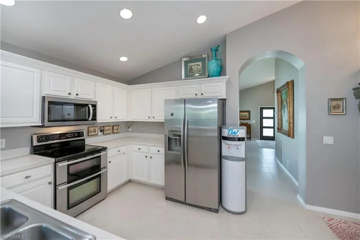 Kitchen with stainless steel appliances, vaulted ceiling, arched walkways, light tile patterned floors, and white cabinetry