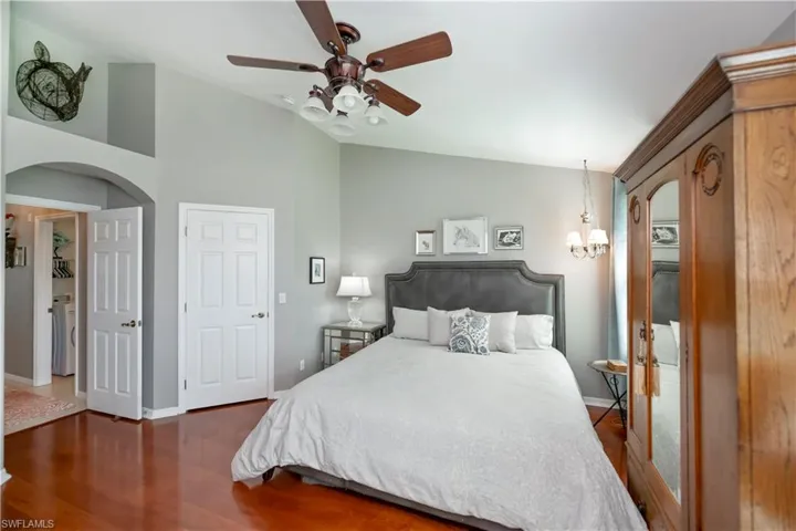 Bedroom with arched walkways, lofted ceiling, wood finished floors, and a ceiling fan