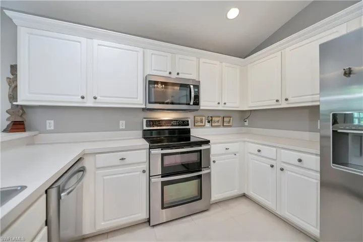 Kitchen with stainless steel appliances, vaulted ceiling, light countertops, white cabinets, and recessed lighting