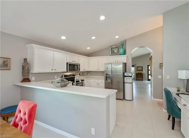 Kitchen featuring appliances with stainless steel finishes, arched walkways, a peninsula, vaulted ceiling, and recessed lighting