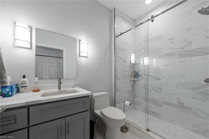 Spa-inspired primary bathroom featuring a frameless glass-enclosed shower with marble-look tile surround, a dark charcoal vanity with white quartz countertop and integrated rectangular sink, chrome fixtures, recessed lighting, and a separate toilet compartment