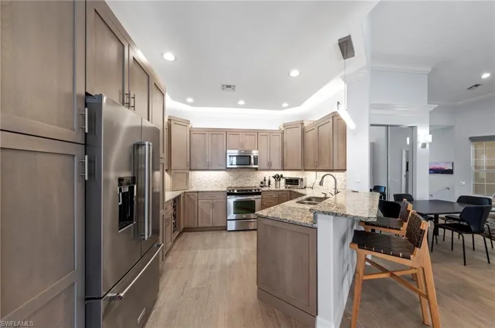 Spacious kitchen featuring warm wood-finish cabinetry, stainless steel appliances including a dual-door refrigerator and gas range, granite countertops, and a large center island with seating