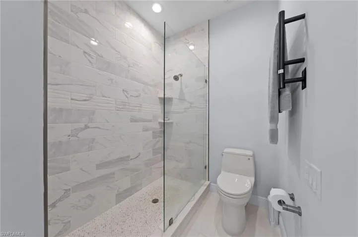 Modern bathroom featuring a frameless glass-enclosed shower with marble-look tile surround, ceramic vessel toilet, and brushed black towel warming rack