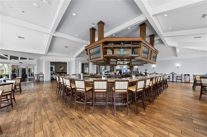 Expansive bar area featuring wood-finish flooring, a large wrap-around bar with seating, a coffered ceiling, recessed lighting, and wall sconces