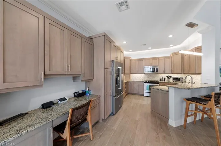 Spacious kitchen featuring custom wood cabinetry, granite countertops, stainless steel appliances, and a large island with seating