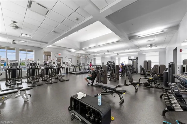 Spacious fitness center featuring a wide array of cardio and strength training equipment, rubberized flooring, ceiling fans, and large windows
