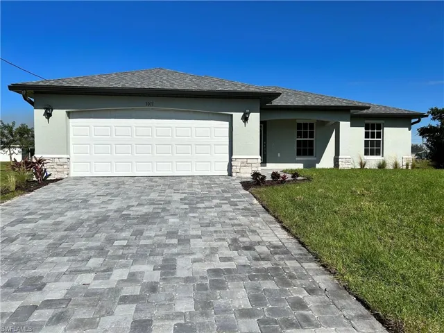 View of front of house with stone siding, a front yard, stucco siding, decorative driveway, and a shingled roof