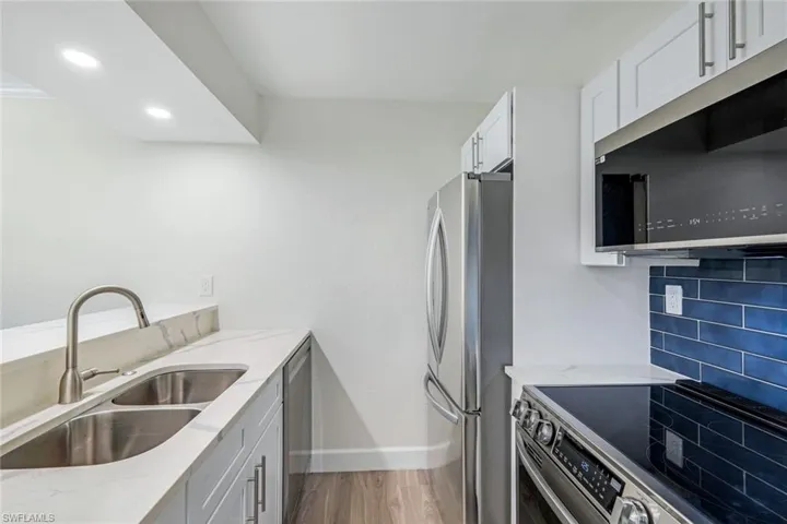 Kitchen featuring appliances with stainless steel finishes, light stone countertops, wood finished floors, white cabinetry, and recessed lighting