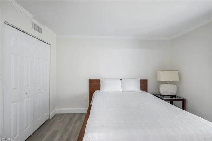Bedroom with wood finished floors, ornamental molding, and a closet
