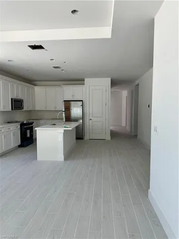 Kitchen featuring light hardwood / wood-style floors, white cabinets, stove, and a center island with sink
