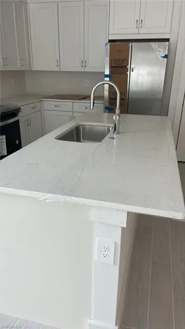 Kitchen with white cabinets, a kitchen island with stainless steel farmhouse sink, light stone counters, stainless steel refrigerator, and sink