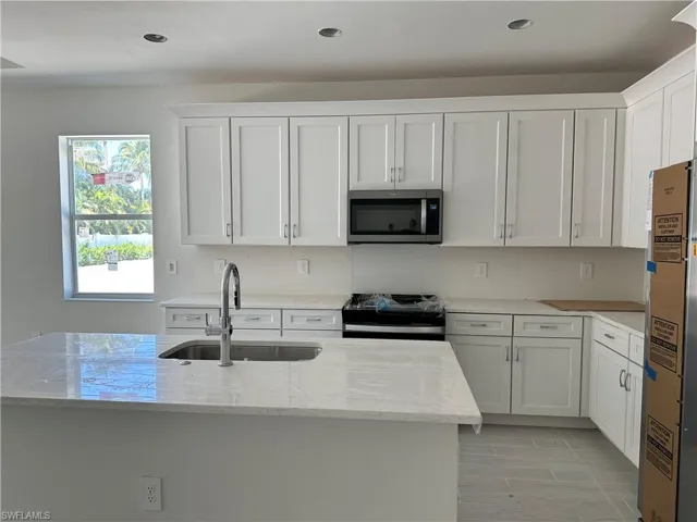 Kitchen featuring white cabinetry, light stone countertops, a kitchen island, stainless steel appliances, and sink