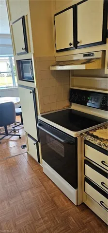 Kitchen with range, dark parquet flooring, ventilation hood, and backsplash