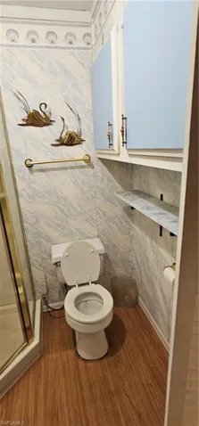 Bathroom with an enclosed shower, tile walls, hardwood / wood-style flooring, and toilet