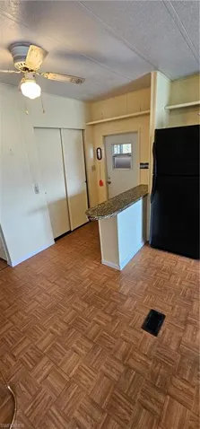 Kitchen with a textured ceiling, ceiling fan, kitchen peninsula, dark parquet flooring, and fridge