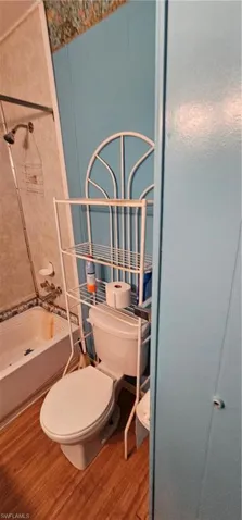 Bathroom with tub / shower combination, toilet, and hardwood / wood-style floors