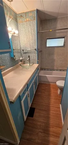 Full bathroom with hardwood / wood-style floors, vanity, tiled shower / bath, and toilet