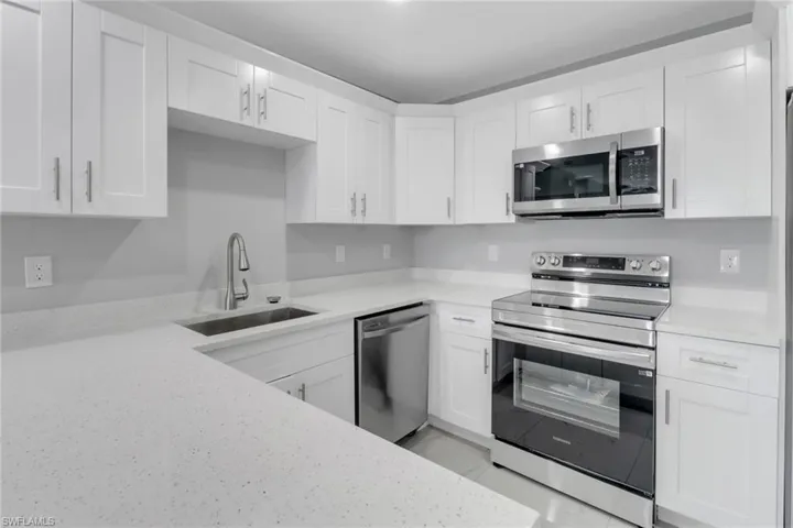 Kitchen featuring appliances with stainless steel finishes, a sink, white cabinetry, and light stone counters