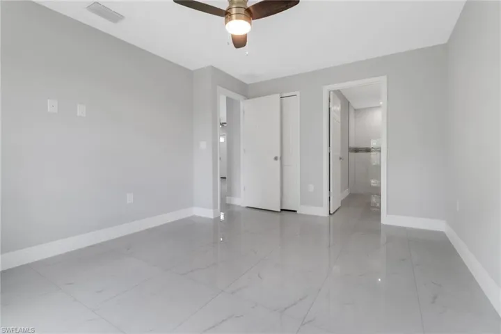 Unfurnished bedroom with marble finish floors, baseboards, connected bathroom, and a ceiling fan