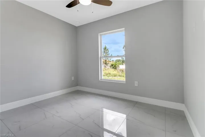 Empty room with marble look tile flooring, baseboards, and a ceiling fan