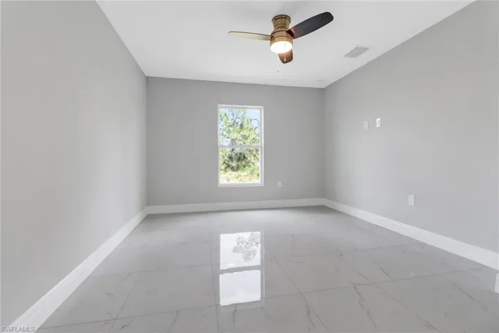 Spare room featuring light marble finish floors, baseboards, and ceiling fan