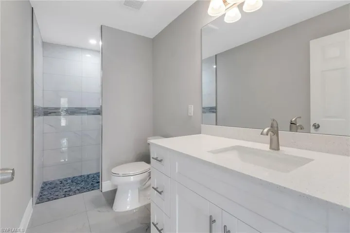 Full bathroom featuring marble finish flooring, toilet, a walk in shower, vanity, and baseboards