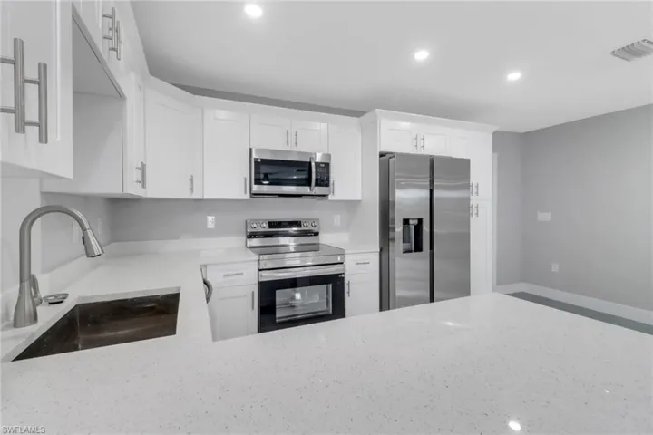 Kitchen with appliances with stainless steel finishes, a sink, light stone counters, and recessed lighting