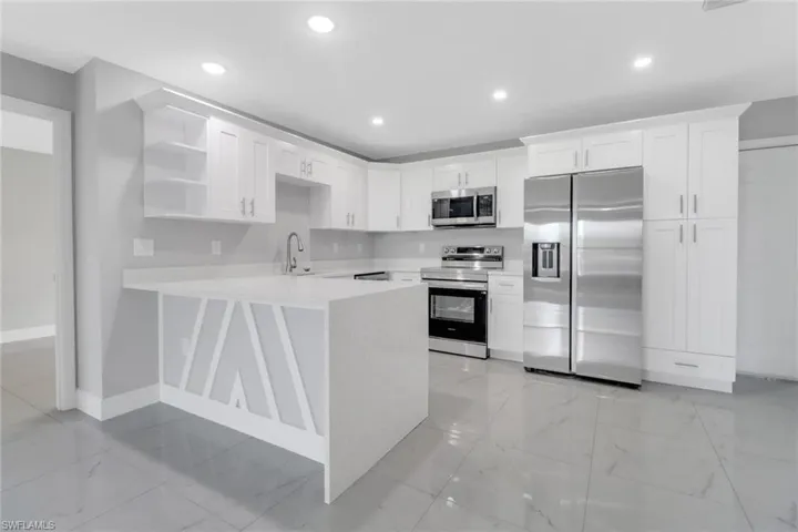 Kitchen featuring appliances with stainless steel finishes, open shelves, light countertops, a peninsula, and baseboards