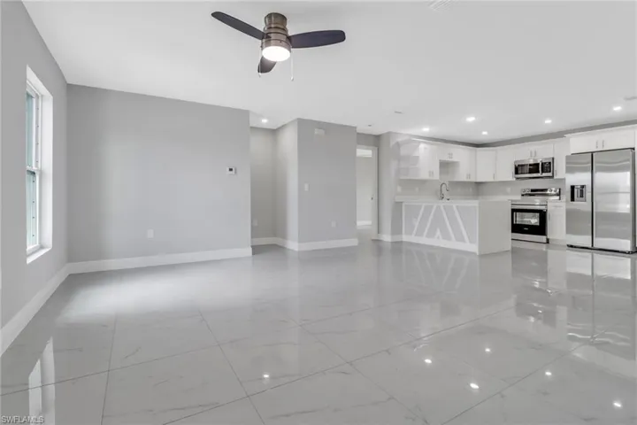 Unfurnished living room featuring baseboards, ceiling fan, recessed lighting, a sink, and light marble finish flooring