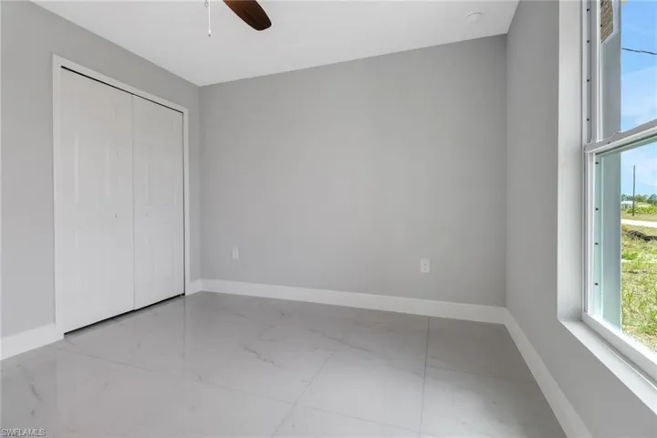 Unfurnished bedroom featuring marble look tiles, baseboards, multiple windows, and a closet