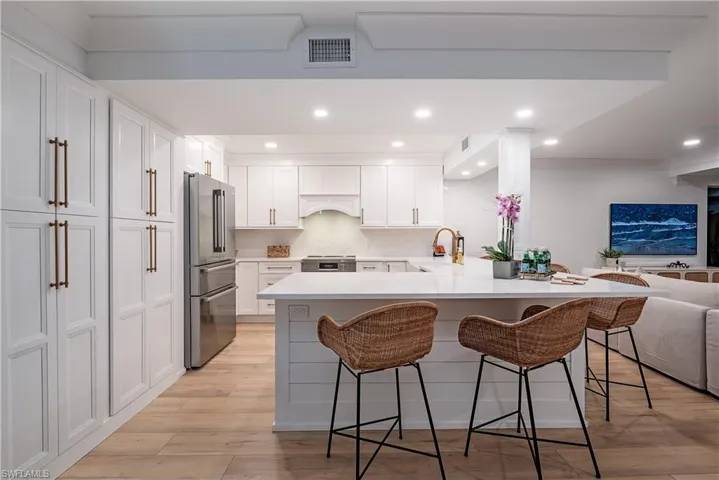Kitchen featuring a kitchen bar, tasteful backsplash, white cabinetry, light hardwood / wood-style flooring, and high end refrigerator