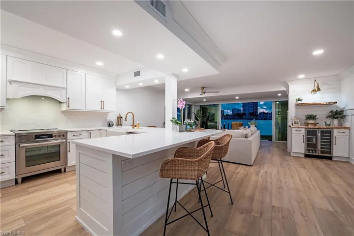 Kitchen with wine cooler, light wood-type flooring, a kitchen bar, stainless steel stove, and kitchen peninsula