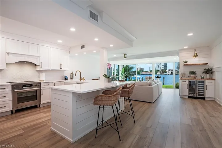 Kitchen with light hardwood / wood-style flooring, white cabinets, backsplash, electric stove, and wine cooler