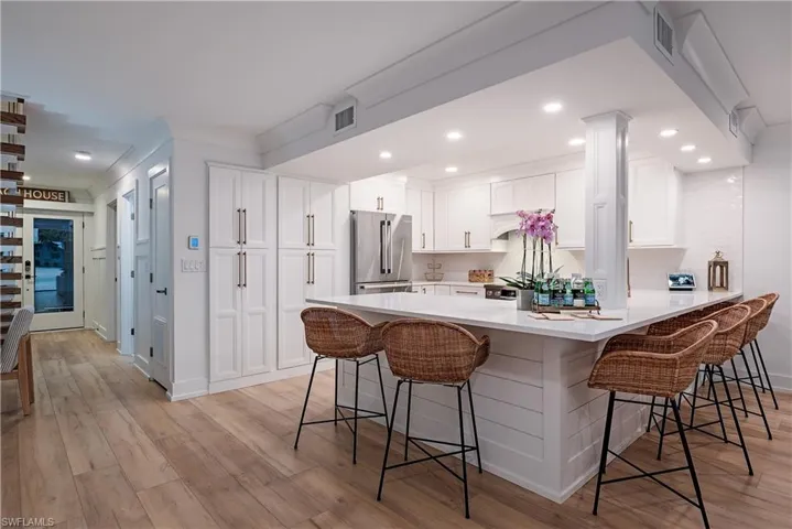 Kitchen with light hardwood / wood-style flooring, a kitchen breakfast bar, high end refrigerator, and white cabinetry