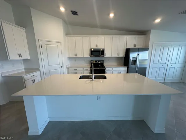 Kitchen with vaulted ceiling, stainless steel appliances, an island with sink, white cabinets, and sink