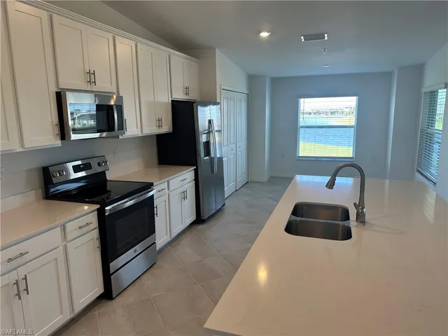 Kitchen with white cabinets, stainless steel appliances, light tile patterned flooring, and sink