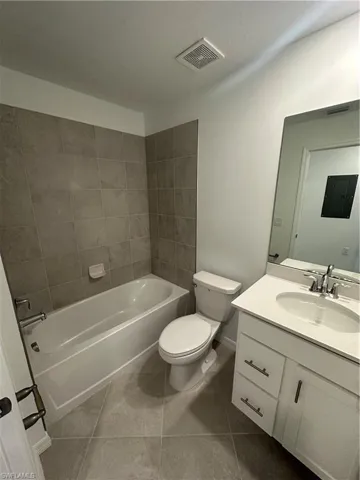 Full bathroom featuring toilet, electric panel, tile patterned flooring, tiled shower / bath, and vanity