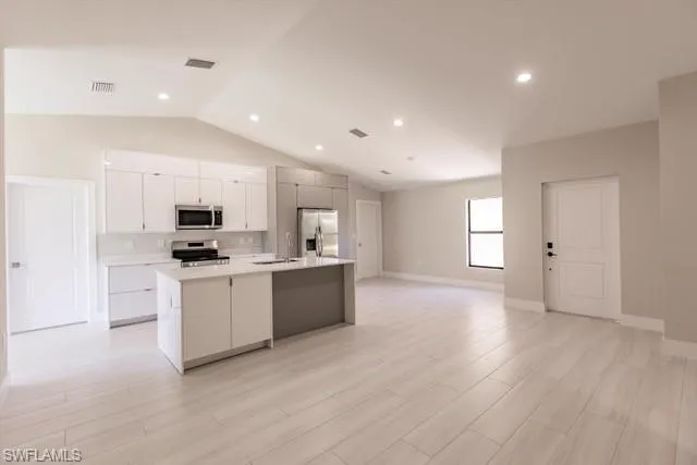 Kitchen with a kitchen island with sink, white cabinets, sink, light hardwood / wood-style floors, and stainless steel appliances