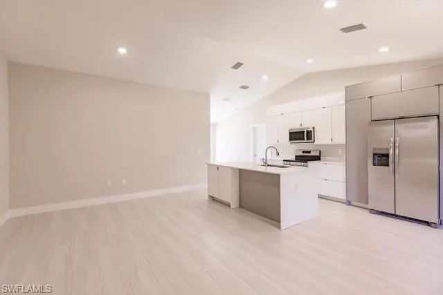 Kitchen featuring light wood-type flooring, stainless steel appliances, sink, a center island with sink, and white cabinetry