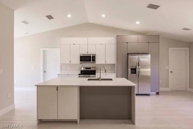 Kitchen featuring white cabinetry, sink, stainless steel appliances, vaulted ceiling, and a kitchen island with sink
