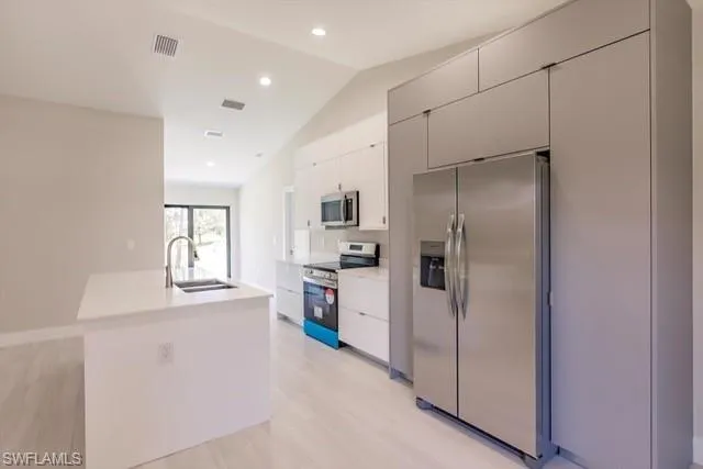 Kitchen featuring white cabinetry, sink, vaulted ceiling, appliances with stainless steel finishes, and light wood-type flooring