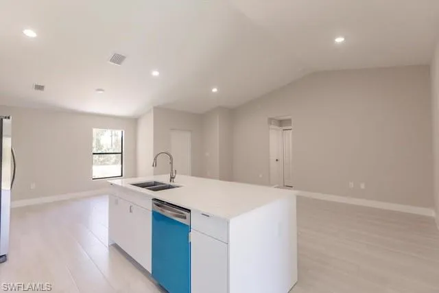 Kitchen featuring a kitchen island with sink, white cabinets, sink, vaulted ceiling, and stainless steel appliances