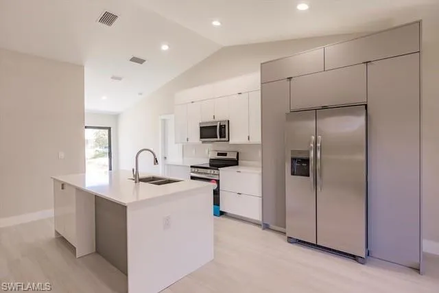 Kitchen with white cabinets, sink, appliances with stainless steel finishes, and an island with sink