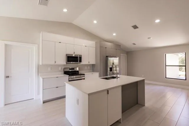 Kitchen with sink, an island with sink, vaulted ceiling, white cabinets, and appliances with stainless steel finishes