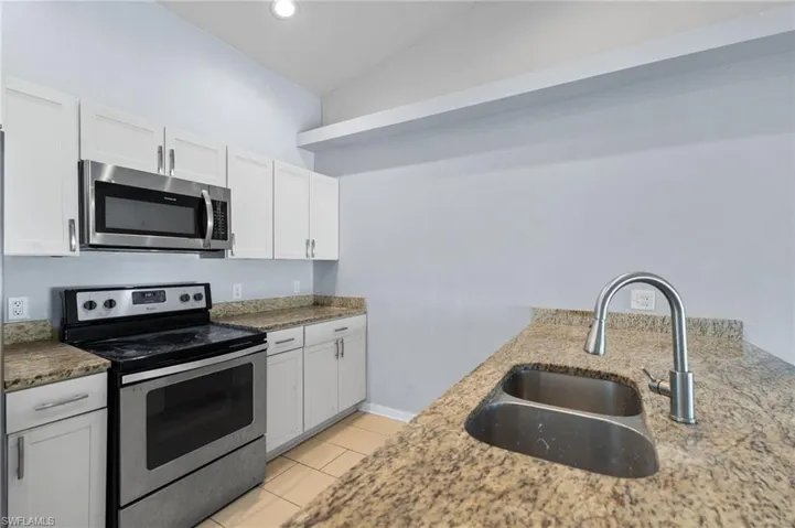 Kitchen with stainless steel appliances, white cabinetry, light stone countertops, and light tile patterned floors