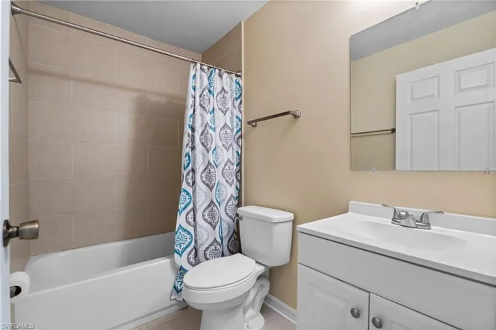 Full bath featuring vanity, shower / bath combo with shower curtain, and light tile patterned flooring