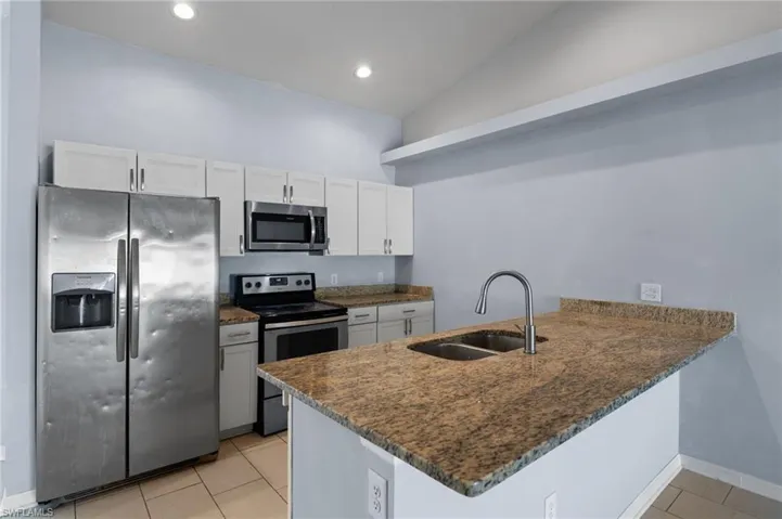 Kitchen featuring appliances with stainless steel finishes, white cabinets, dark stone countertops, light tile patterned floors, and recessed lighting